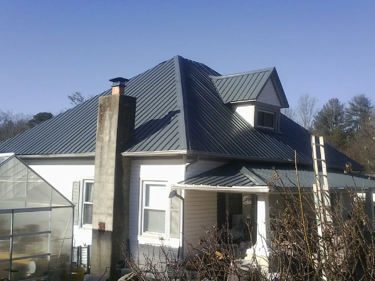 Dark blue standing seam metal roof on a white farmhouse with dormer — Slate & Tile Roof Repair by Roofing Brothers in Rhodes