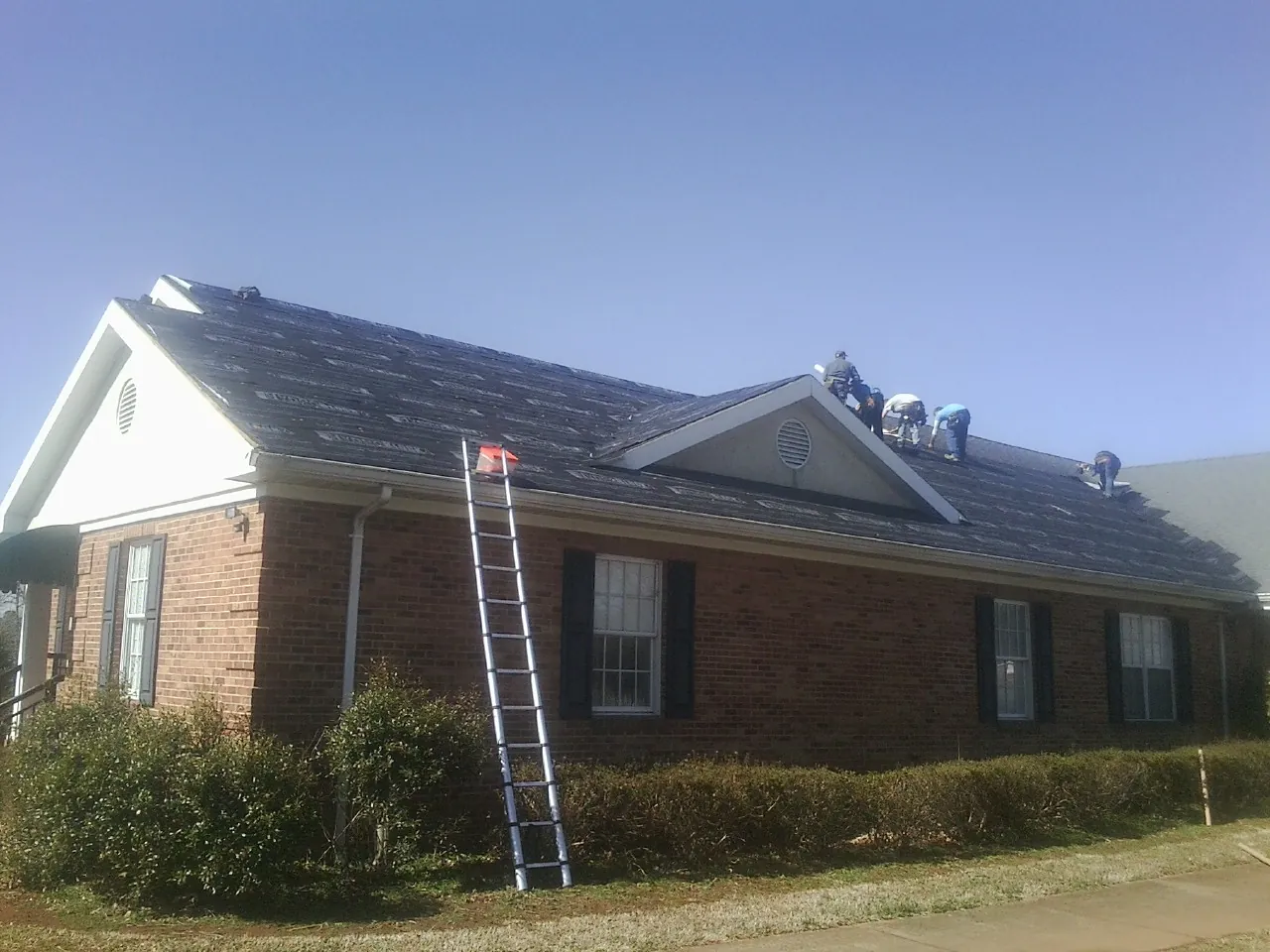 Crew tearing shingles off a brick ranch roof with a ladder set — Emergency Roof Repair work by our crew in Rhodes