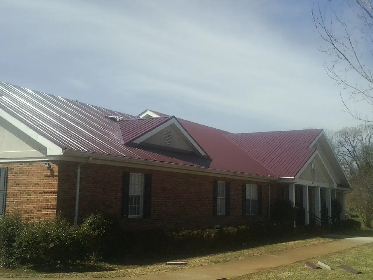 Red metal roof with gabled entries on a long brick building, from a Hail Damage Roof Repair job in Rhodes