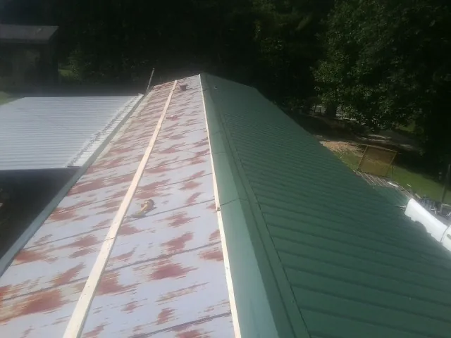 Old rusted panels beside newly installed green metal roofing — Wind Damage Roof Repair by Roofing Brothers in Rhodes