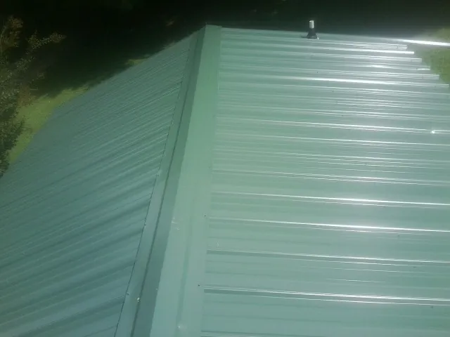 New green metal panels meeting at the ridge of a roof — Flat Roof Repair work by our crew in Rhodes