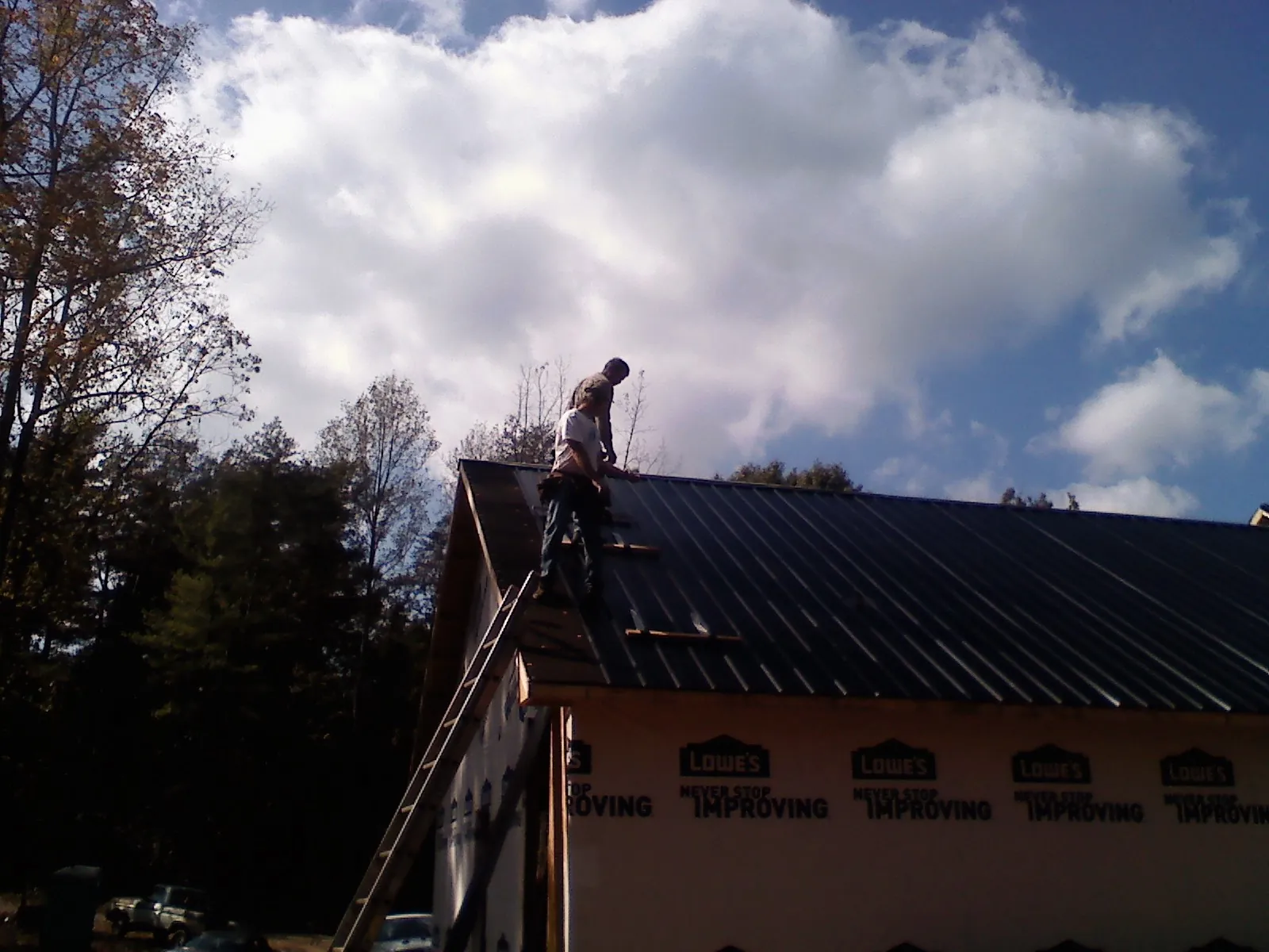 Roofer fastening dark metal panels high against a cloudy sky, from a Roof Inspection job in Rhodes