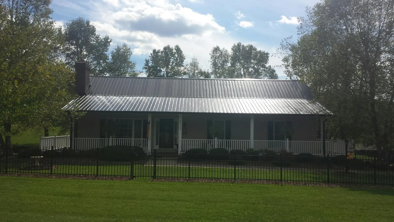 Gray metal roof on a brick ranch with a full width front porch — Gutter Guard Installation work by our crew in Rhodes