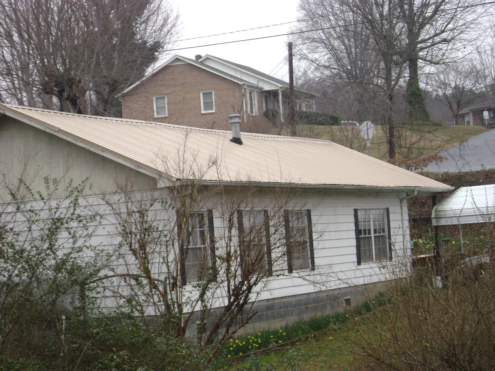 Tan metal roof on a white sided house set into a hillside — Commercial Roofing by Roofing Brothers in Rhodes