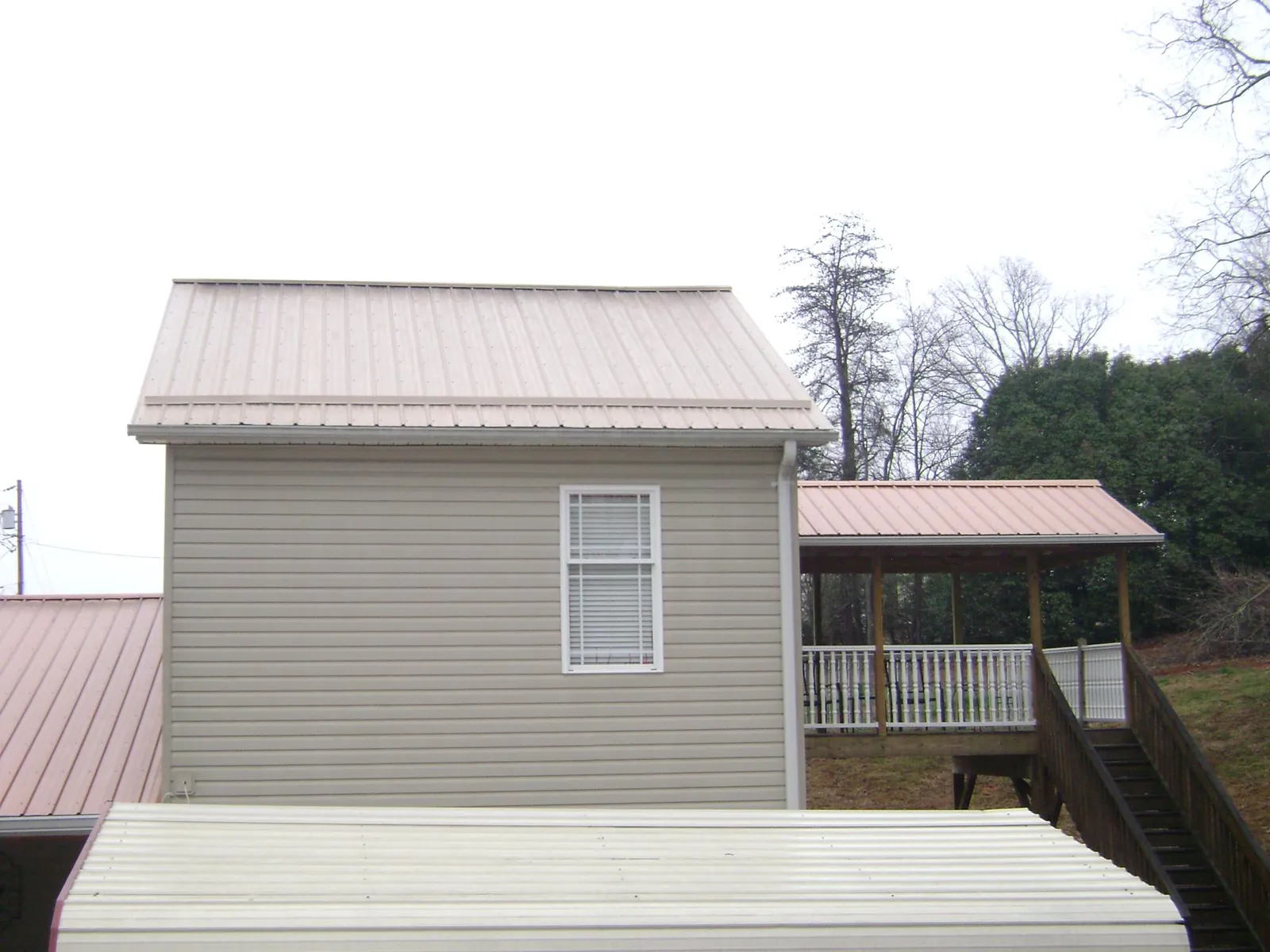 Tan metal roofs on a two story addition and attached porch, from a Roof Replacement job in Rhodes